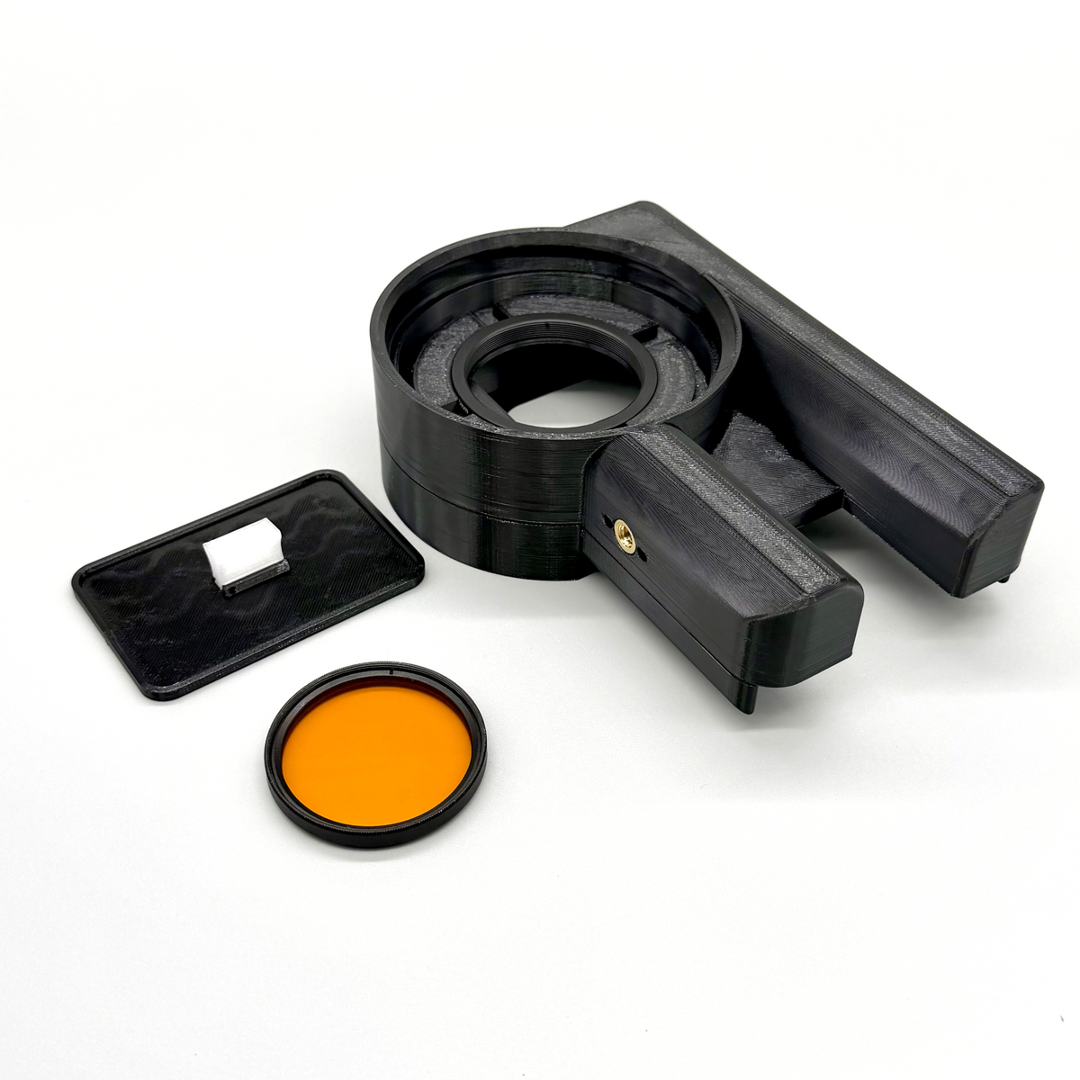 Porthole Creator Cradle for iPhone and Android. Black camera lens hood with an orange filter on a white background. Black coffee filter holder with a brown filter on a white background. Black camera lens filter holder with an orange filter on a white background