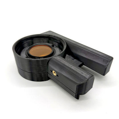 Porthole Creator Cradle for iPhone and Android. Black camera lens hood with an orange filter on a white background. Black coffee filter holder with a brown filter on a white background